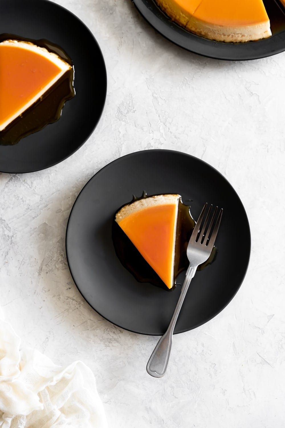 slices of cream cheese flan on dark gray plates on a white background