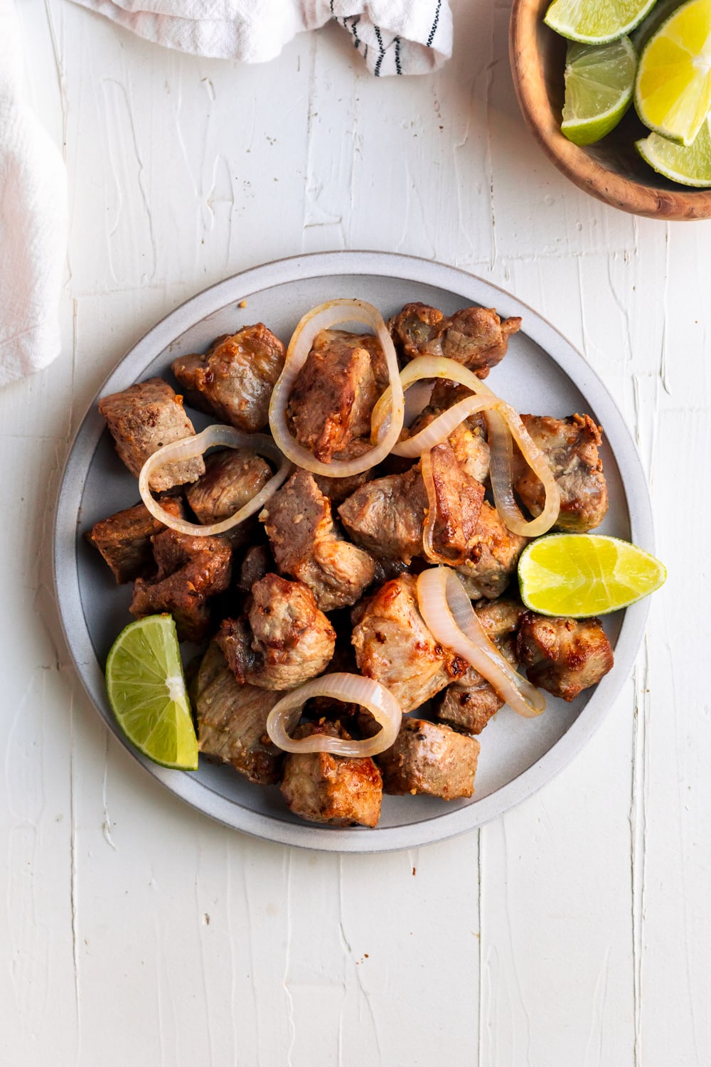 a plate with juicy, tender Cuban masitas de puerco with onions and lime wedges