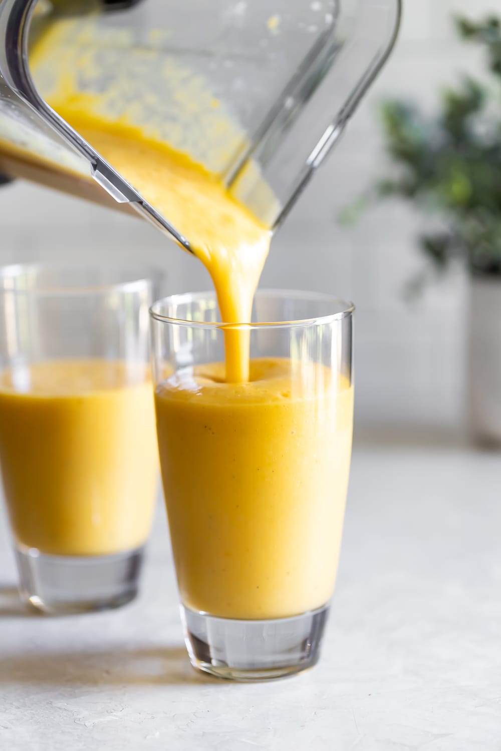 pouring batido de mango into a large glass from blender