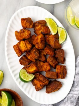 An overhead shot of chicharrones de puerco on a white platter with lime slices on the side on a white counter.