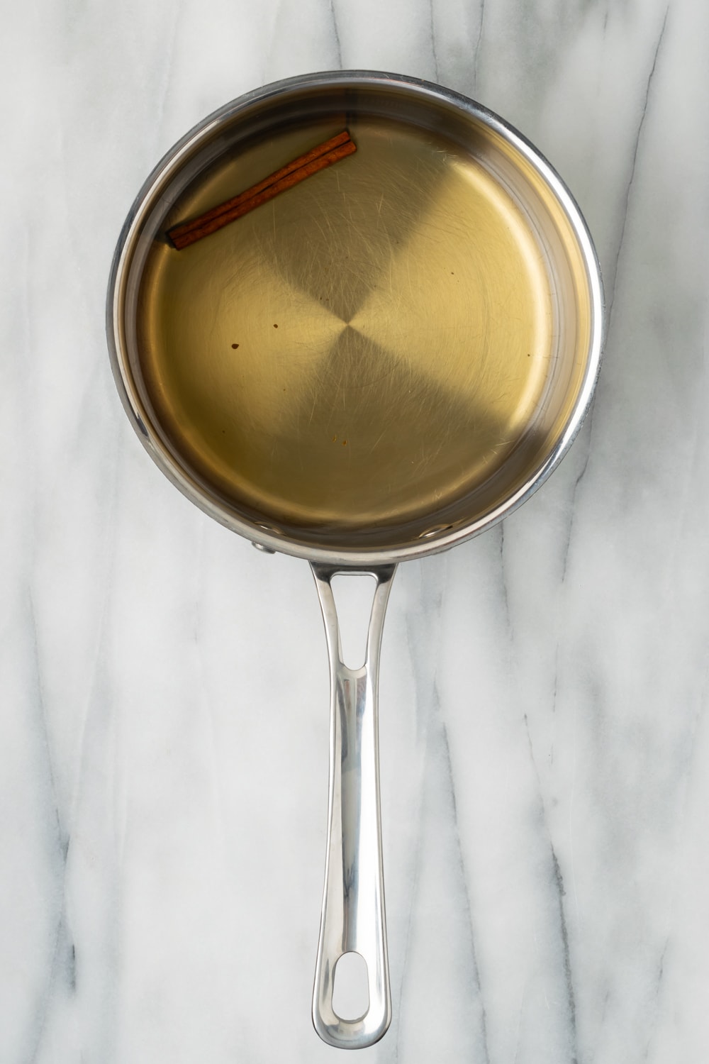 An overhead shot of a saucepan with water, cinnamon stick, and brown sugar making a syrup for empanada dough