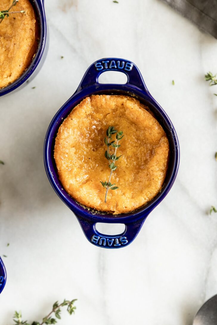 Golden baked cheesecake in a blue Staub ramekin with thyme garnish, perfect for dessert lovers.