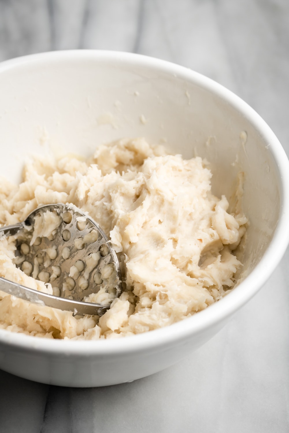 mashing the boiled yuca and malanga into a dough in a white bowl
