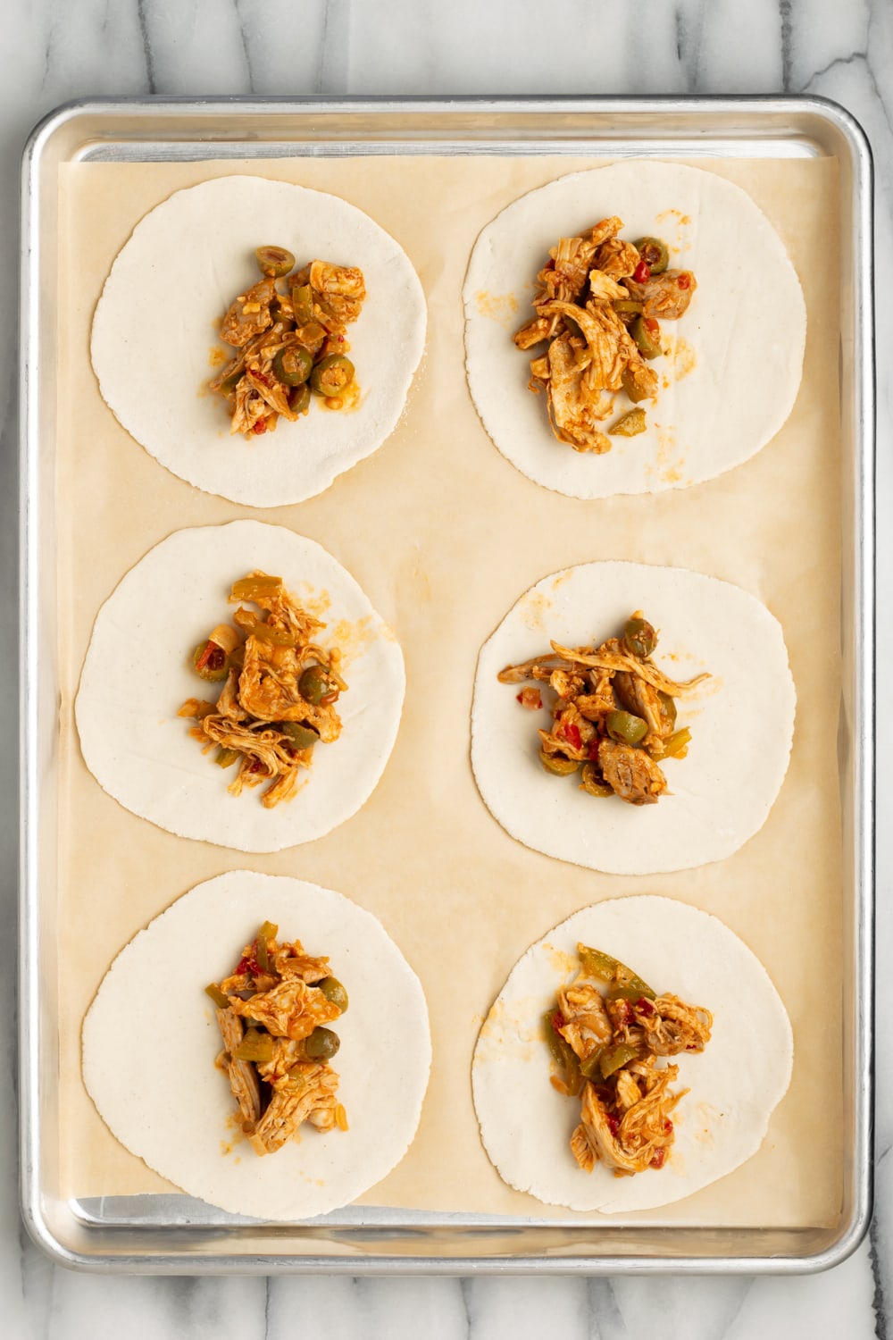 Empanada dough discs filled with cuban chicken filling that haven't been sealed yet.