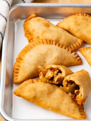 Chicken Empanadas on a parchment lined baking sheet one empanada is broken in half