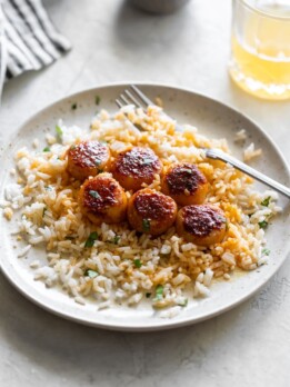 a white plate scallops tossed in spices with garlic butter served over white rice