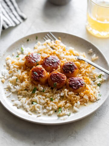 a white plate scallops tossed in spices with garlic butter served over white rice