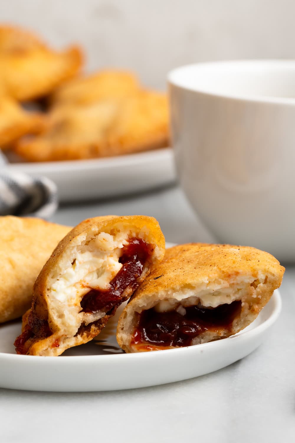 A guava cheese empanada cut in half showing the filling on a white plate with more empanadas in the background.