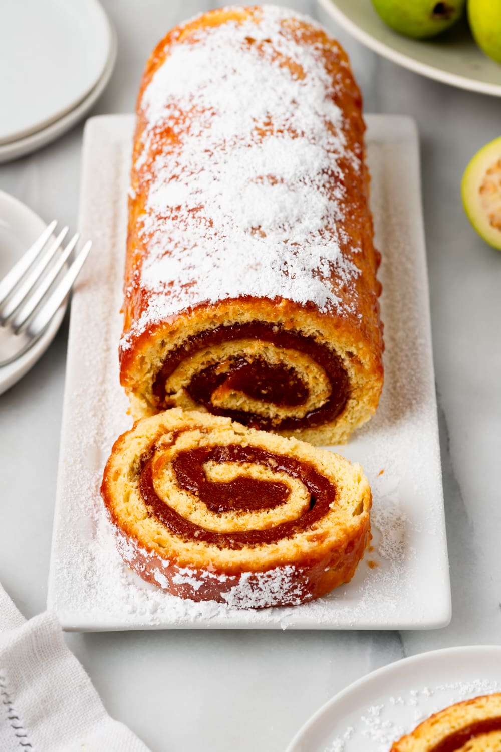 A brazo gutano (guava swiss roll) on a white platter that has a slice cut off and still sitting on the platter