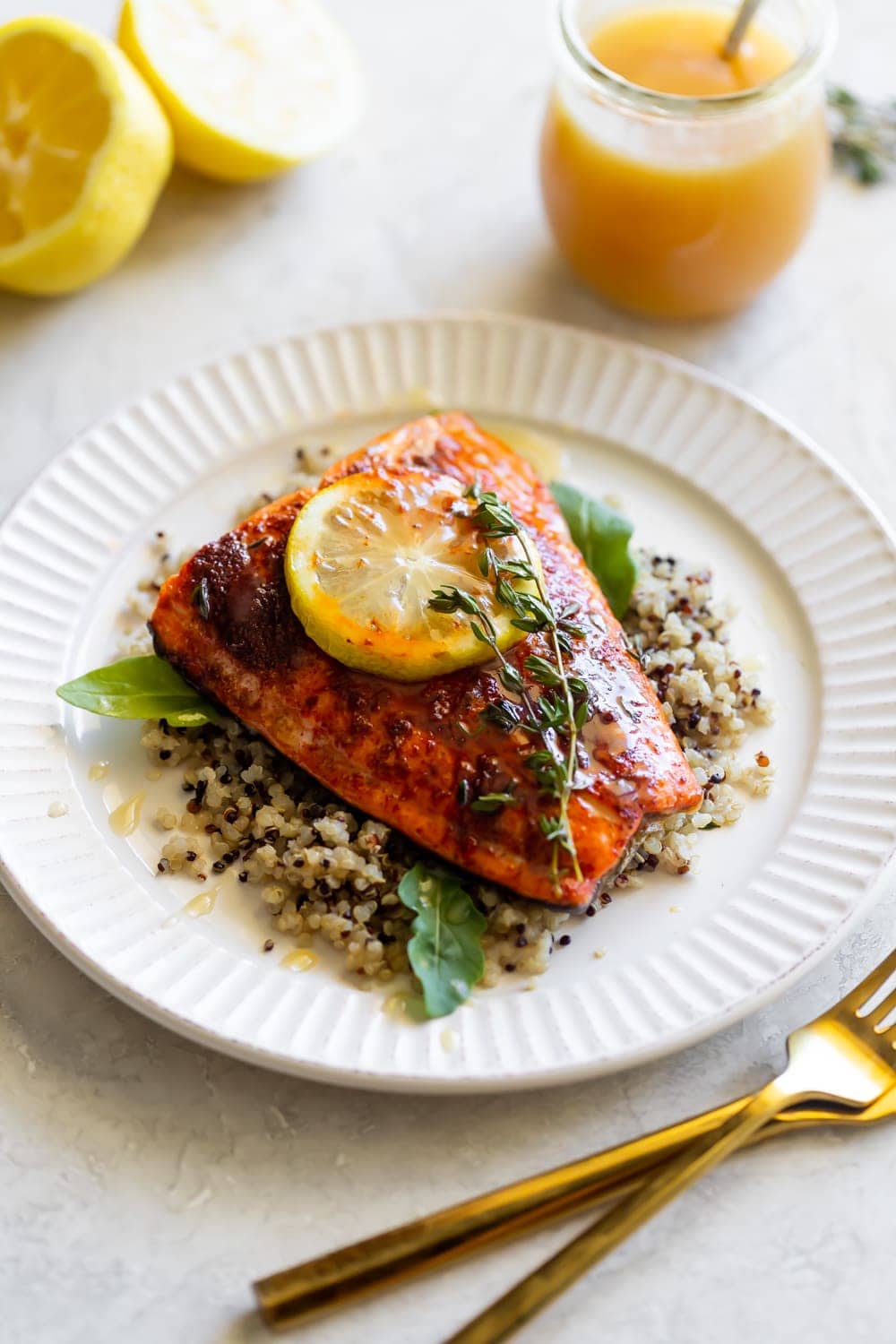 side angle of spicy salmon on a white plate with a lemon slice and fresh thyme