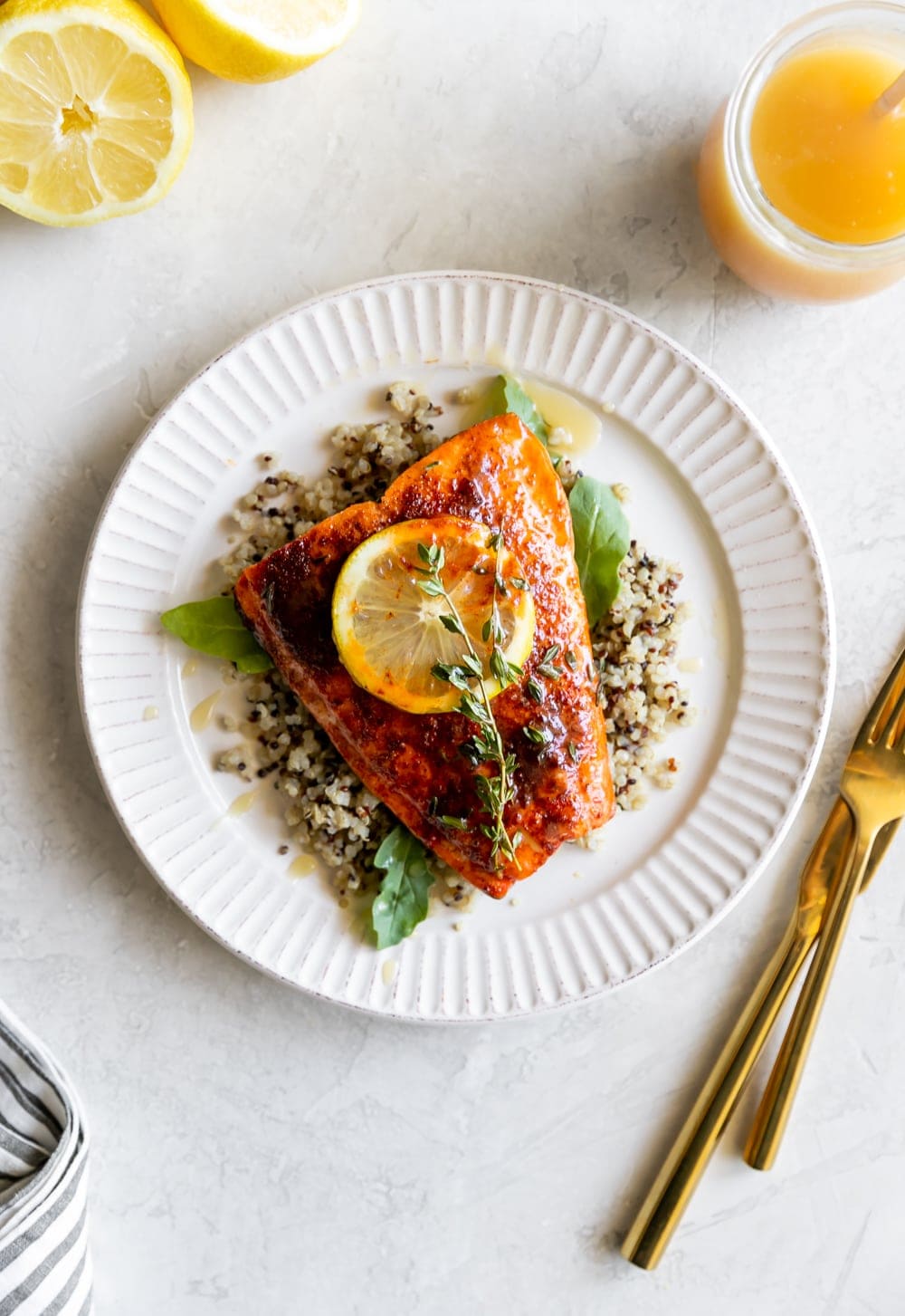 spicy salmon with honey butter on a white plate with a lemon slice and a gold fork and knife
