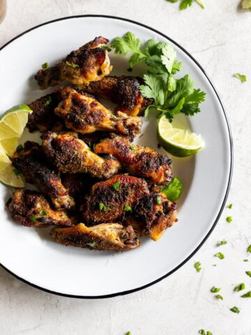 citrus and garlic marinated chicken wings on a plate with lime and cilantro
