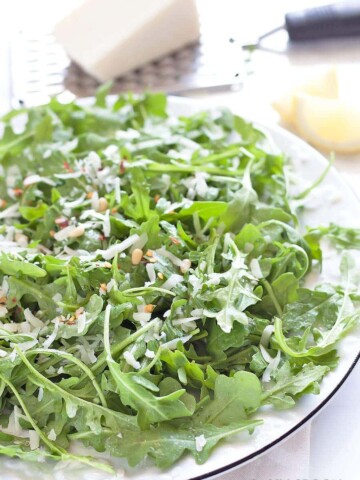 a plate of arugula with pine nuts, lemon dressing, red chili flakes and pecorino