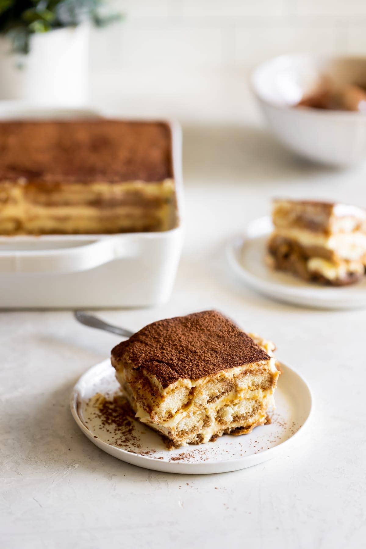 slice of tiramisu on a white plate dusted with cocoa